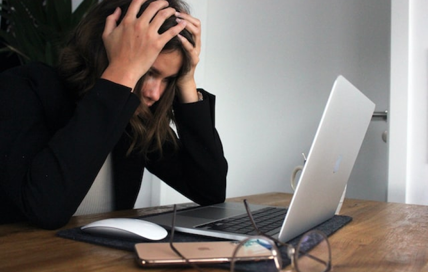 A woman, frustrated and stressed, before a laptop