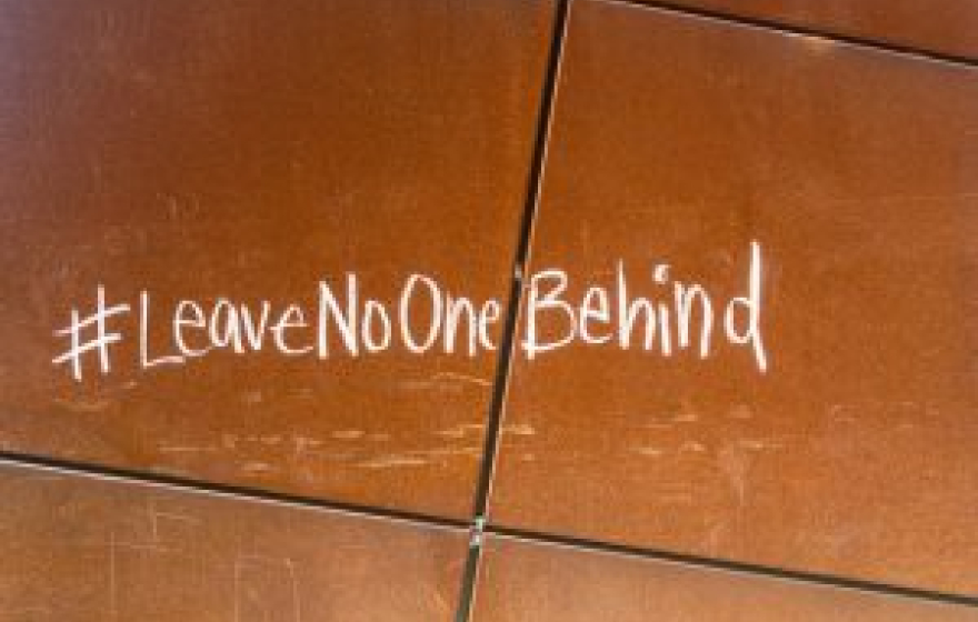 # Leave no one behind written in chalk on a brown tile floor.