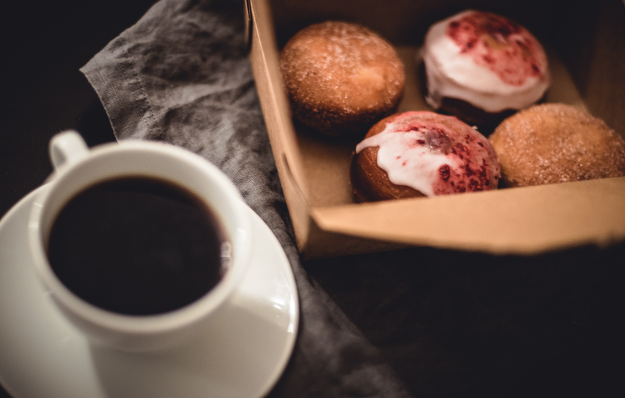 Coffee cup and box of donuts on a table. 
