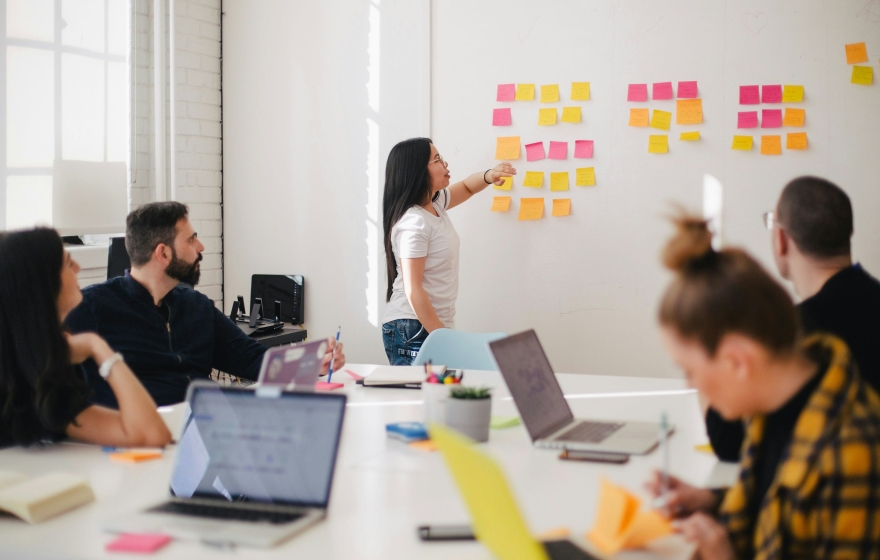 a small group of people working together in a room with laptops and sticky notes and a whiteboard
