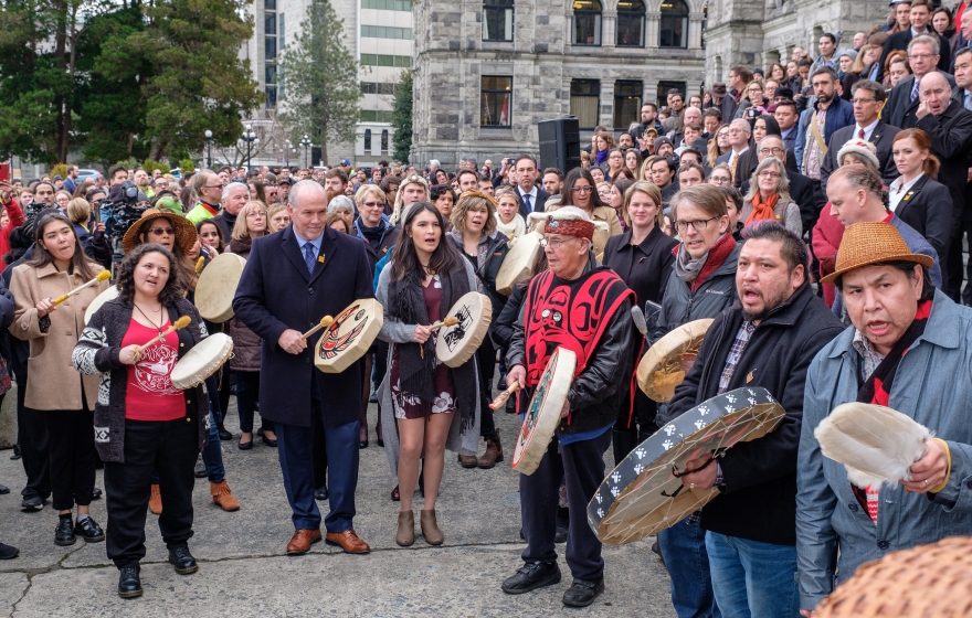 a crowd of people, mostly Indigenous communities and allies, gather and march in the streets with traditional drums