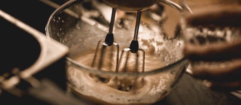Cake batter in a glass bowl being whipped with an electric stand mixer.