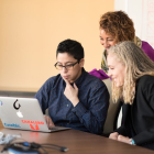 Three women sitting at a table looking at a laptop.