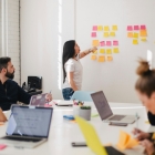 a small group of people working together in a room with laptops and sticky notes and a whiteboard